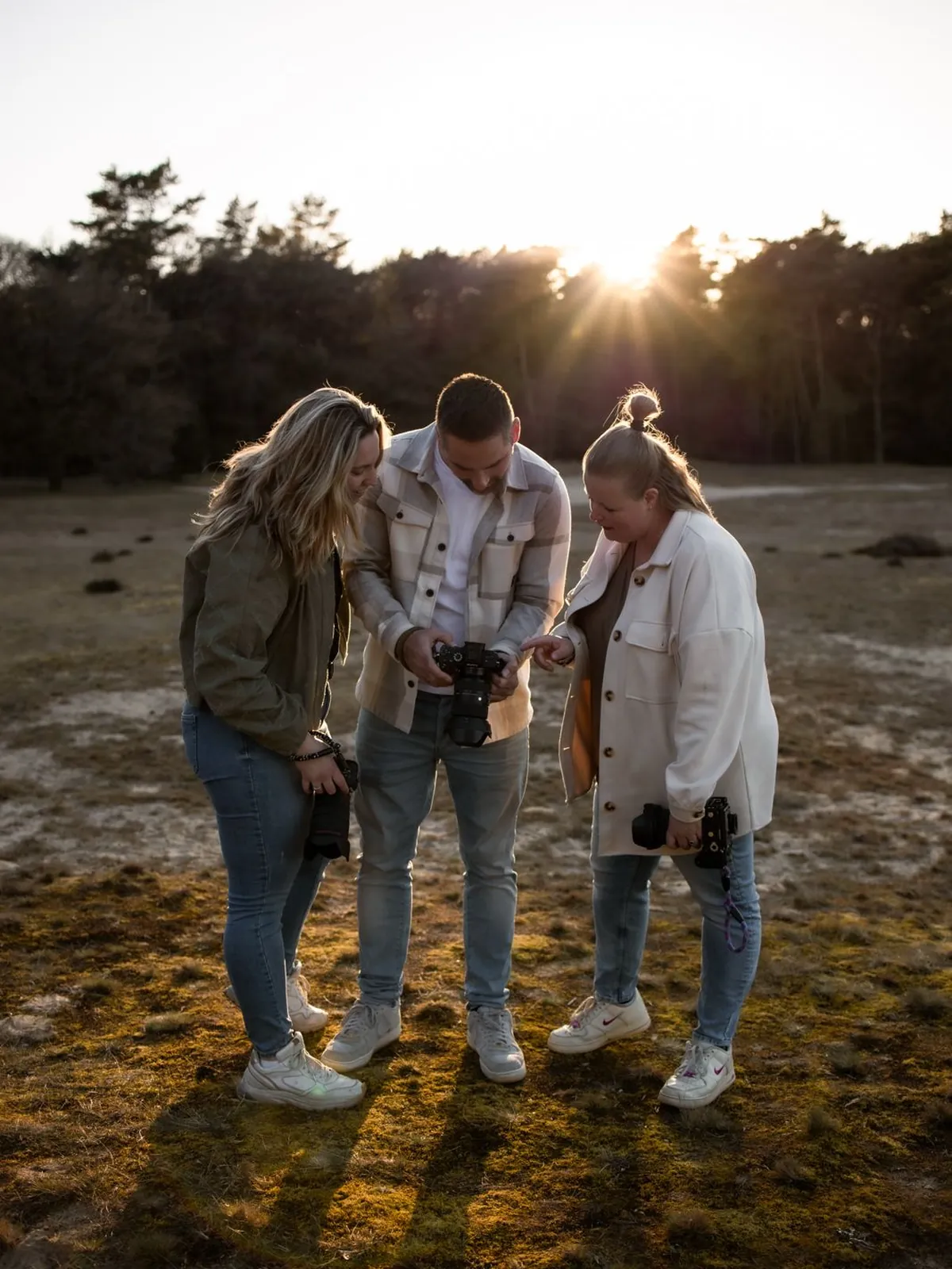 Jolien, Melvin en Sanne kijken samen naar het schermpje van een systeemcamera in de duinen bij zonsondergang